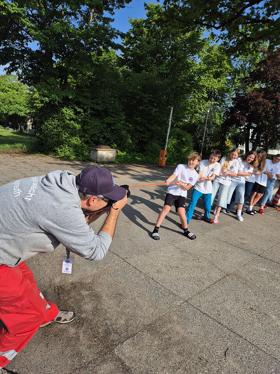 Auf dem Bild ist ein Fotograf zu sehen, der Kinder fotografiert, die einen Strick in der Hand halten und Seilziehen spielen