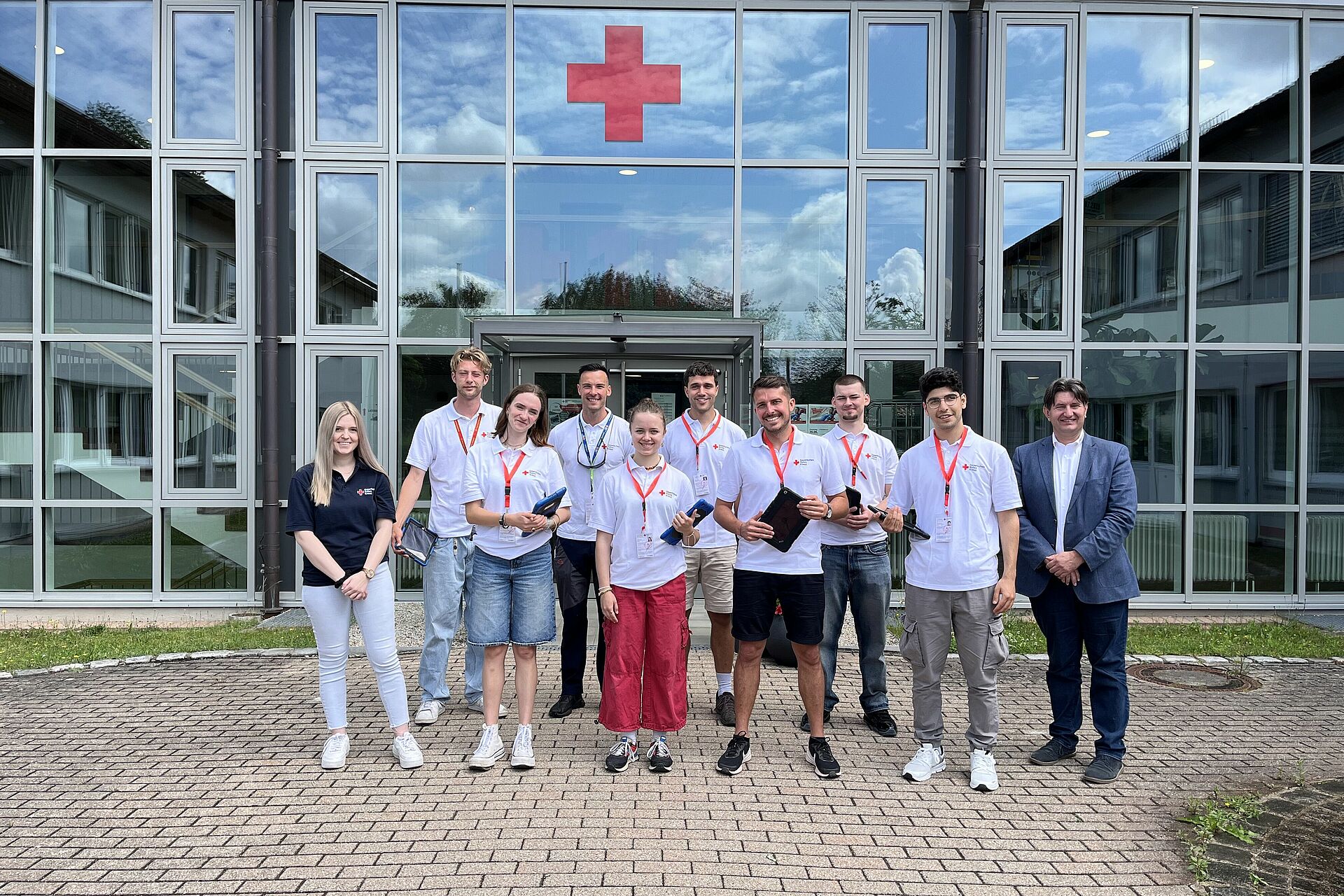Weber in weißen BRK Poloshirts zu sehen, stehend vor dem Haupteingang BRK Weiden, Geschäftsführer und Sachbearbeiterin rechts und links am Bild