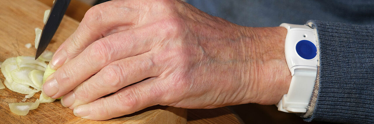 Mann schneidet Zwiebel am Küchenbrett, Hausnotruf Knopf am linken Handgelenk