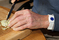 Mann schneidet Zwiebel am Küchenbrett, Hausnotruf Knopf am linken Handgelenk