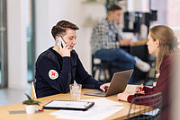 BRK Mitarbeiterin telefoniert am Handy, sie symbilisiert die Ansprechpartnerin für Anfragen, gegenüber sietzt eine Interessentin