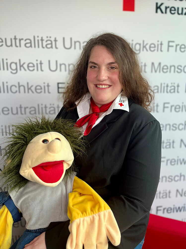 Zeigt Mitarbeitenden mit BRK Oberteil und Kinderhandpuppe