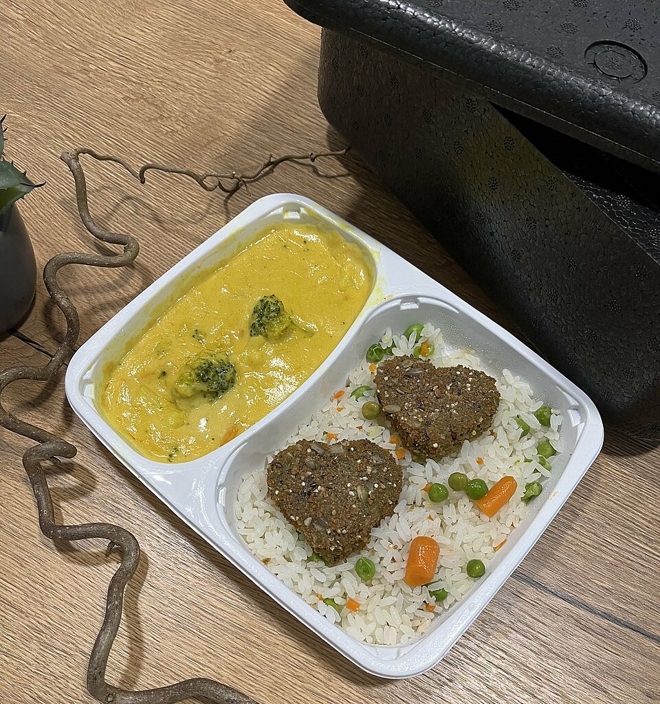 Menü für Essen auf Rädern: Plastikschale mit vegetarischen Gericht, dahinter Wärmebox