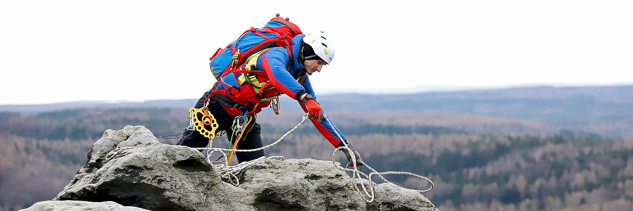 Bergwacht Mitglied steht am Berg und arbeitet mit Seilen