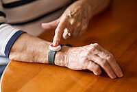 Hände von älterer Dame mit Armband am rechten Hangelenk, Druckknopf für Hausnotruf