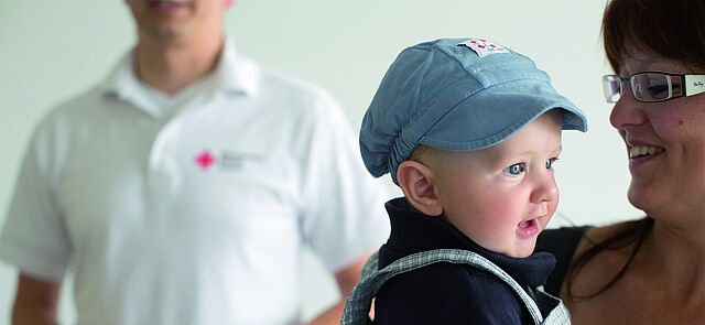 Baby am Arm der Mutter, Erste Hilfe am Kind, Trainer im Hintergrund stehend